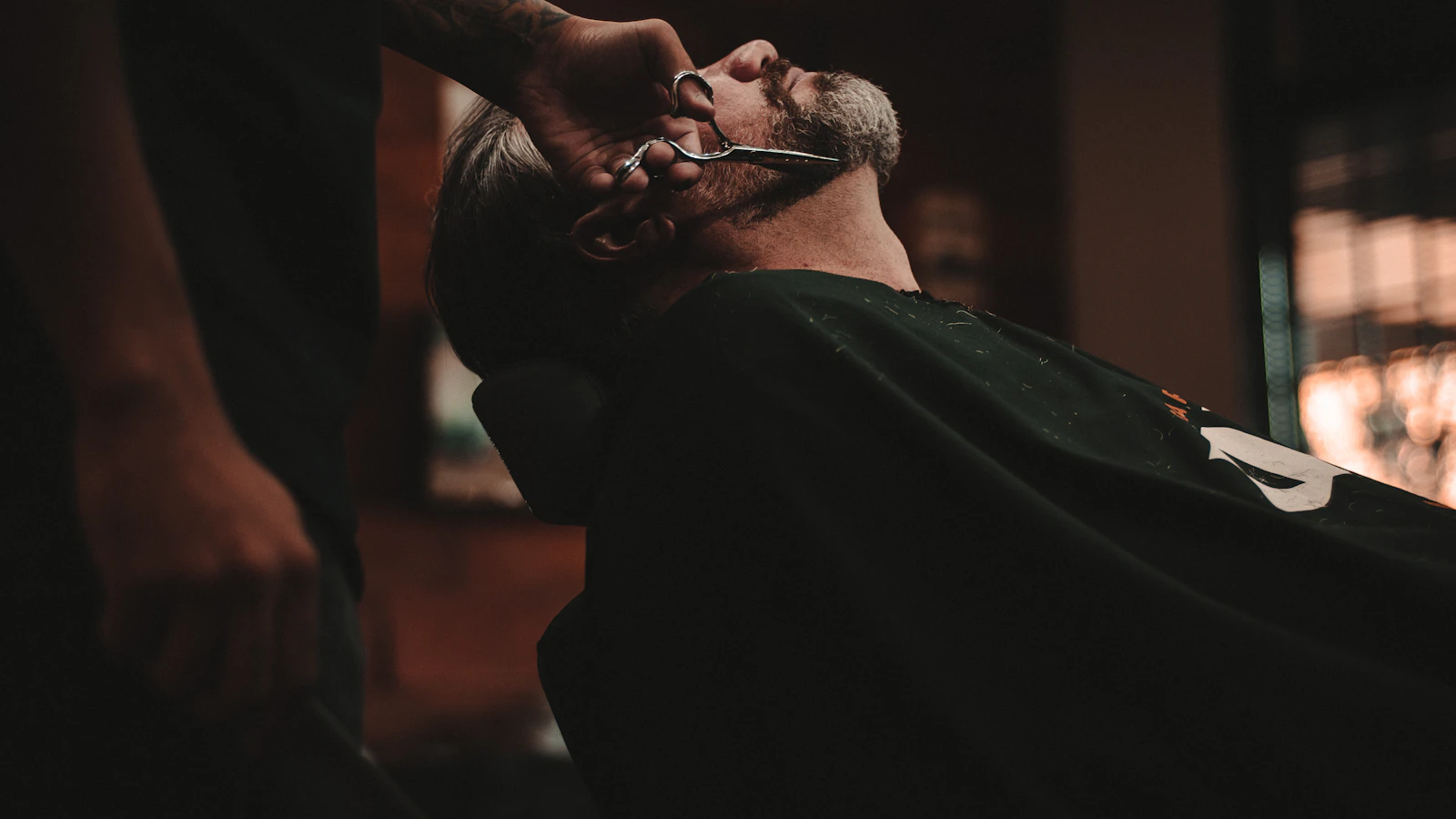 A barber carefully shaping a client’s beard in a warmly lit shop
